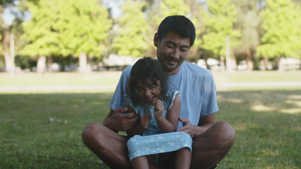 feliz joven padre asiático haciendo cosquillas a su pequeña hija al aire libre