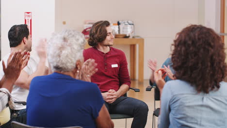 man standing to address self help therapy group meeting in community center