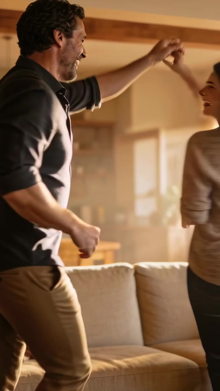 Video verticale: Uomo e donna che si tengono per mano, lui le solleva la mano, lei volteggia vicino al divano in soggiorno per divertimento.