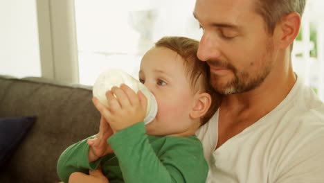 niño en el regazo de su padre bebiendo leche en el sofá en casa 4k