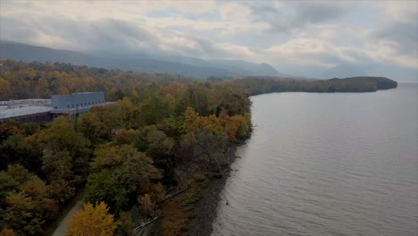 rising-above-colorful-foliage-during-autumn,-alongside-a-river-with-mountains-in-the-background