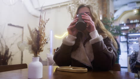 thoughtful lady in brown shearling jacket sipping coffee, immersed in cozy cafe ambiance. soft lighting captures peaceful moment, creating serene atmosphere perfect for relaxation or reflection
