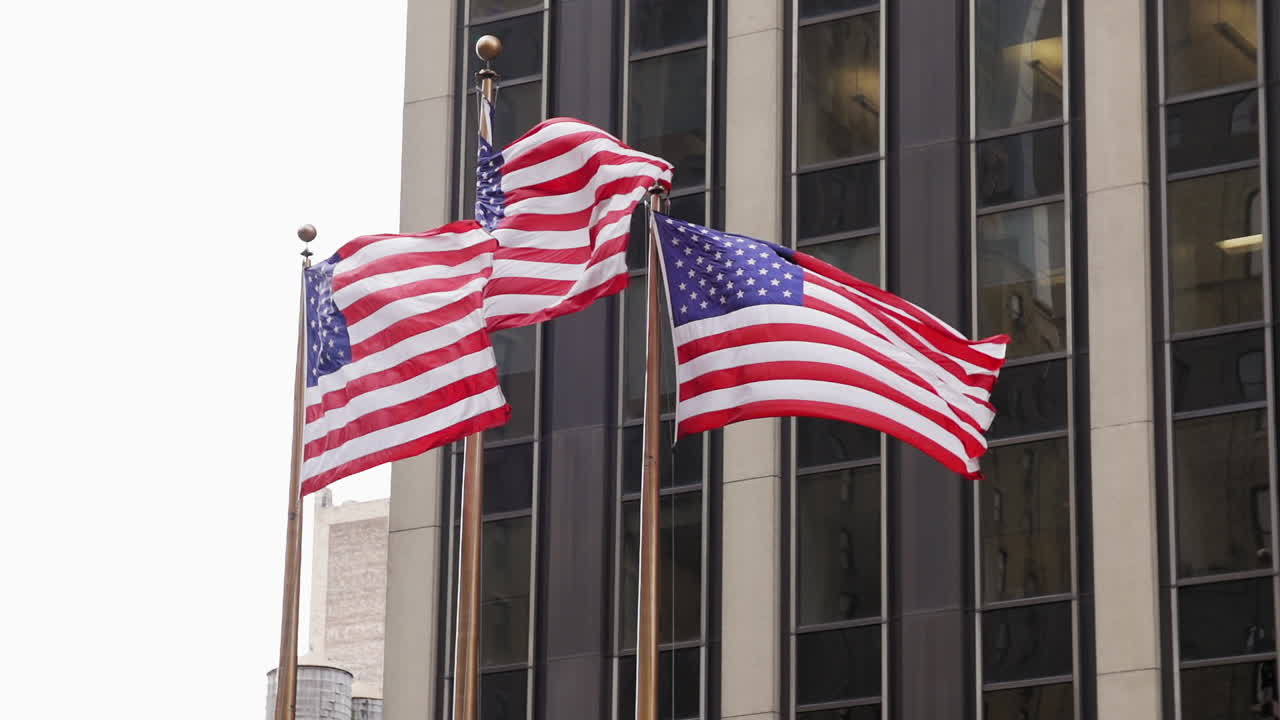Tre bandiere americane che sventolano al vento con un edificio di New York sullo sfondo.