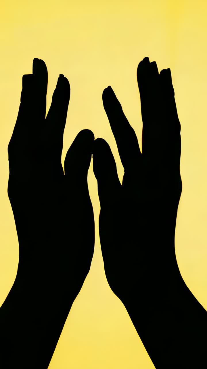 Vertical video: Starting shadow hands moving to meet fingers in studio on yellow panel, clasping