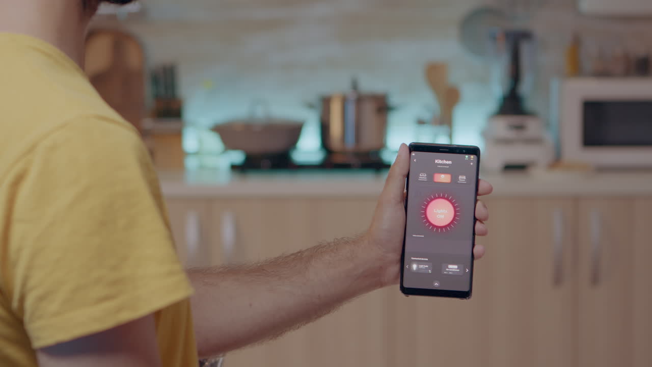Male holding mobile with lighting controlling app sitting in kitchen