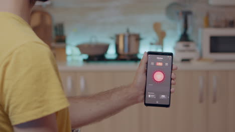 hombre sosteniendo un móvil con una aplicación de control de iluminación sentado en la cocina