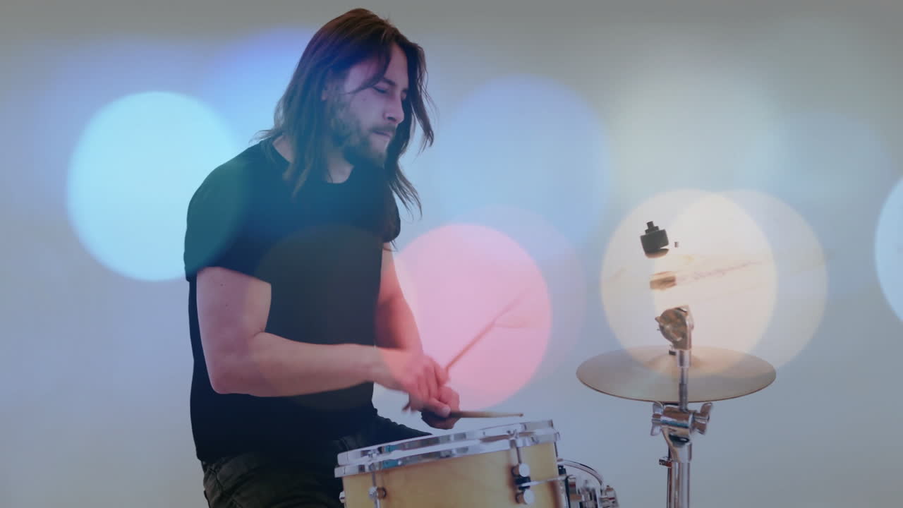 Male drummer playing snare drum and hi-hat in white studio, showing colorful bokeh music graphics