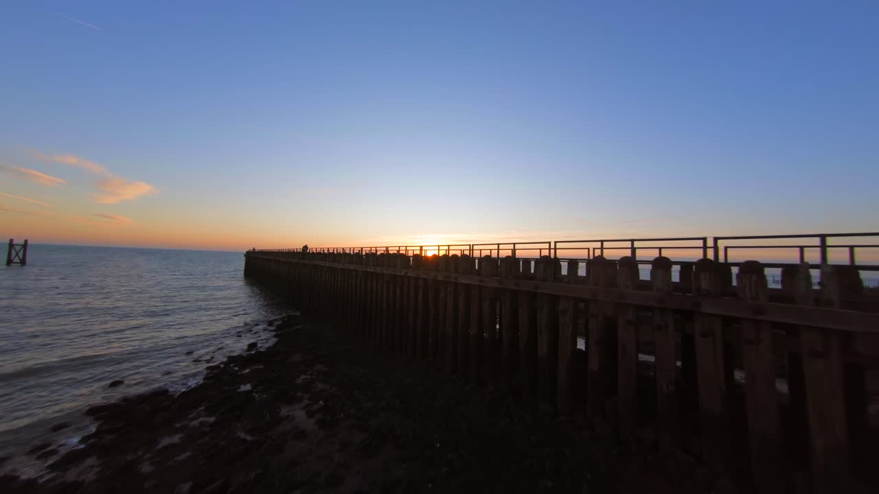 Drone flying over a pier with people revealing the sunset at sea