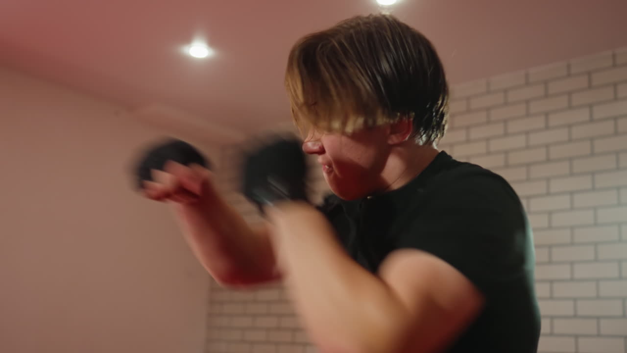 Boxer wearing black shirt trains inside gym, raising fists in defensive stance with intense focus, sweat visible, demonstrating discipline, strength, endurance, and physical conditioning during practice