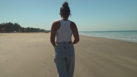 joven morena caminando lentamente a lo largo de la orilla de una playa, horizonte de fondo con agua turquesa