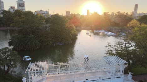 Muñeca-Aérea-Sobre-El-Puente-Blanco-Y-Barcos-Navegando-En-Un-Estanque-En-Los-Jardines-Rosedal-A-La-Hora-Dorada,-Buenos-Aires