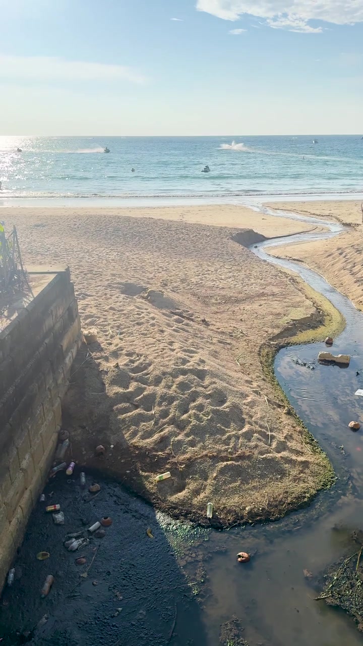 Toma aérea de agua contaminada oscura y basura fluyendo hacia agua de mar tropical clara.
