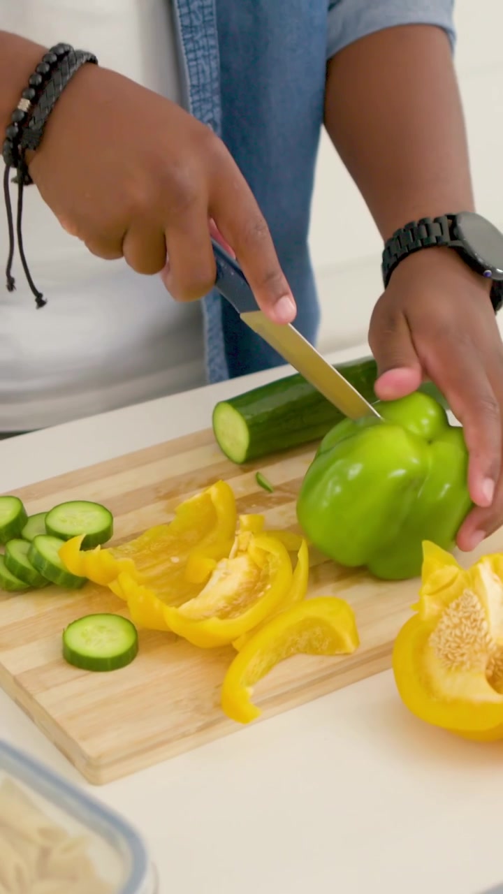 Video verticale: Cuoco casalingo che posiziona e affetta un peperone verde su un tagliere in cucina per la preparazione, in jeans.