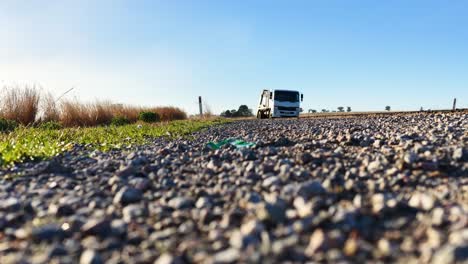 a heavy-duty truck travels along a natural gravel road in the australian countryside, captured from a low, ground-level perspective in bright daylight