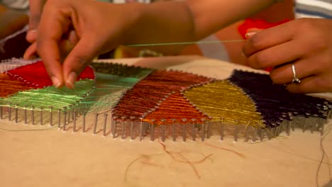una niña de una zona rural de etiopía está haciendo arte con cuerdas con la ayuda de su hermano, tratando de terminar esta paz y lista para vender.