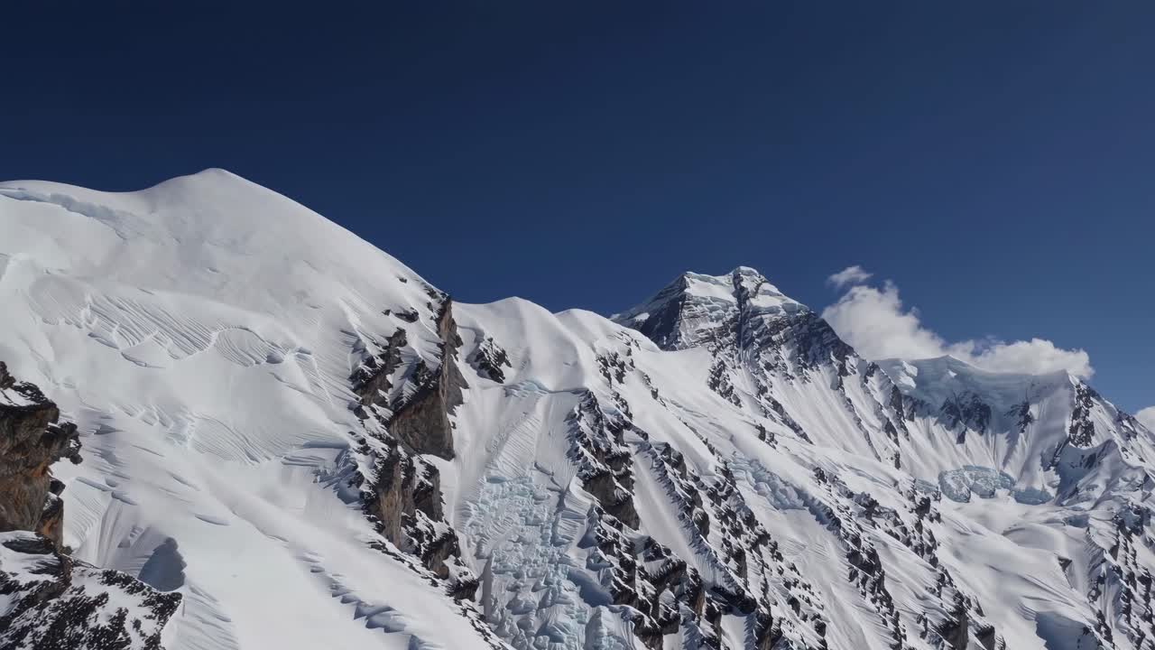 Aerial video view of snow-covered mountain peaks under a clear blue sky, showcasing rugged terrain