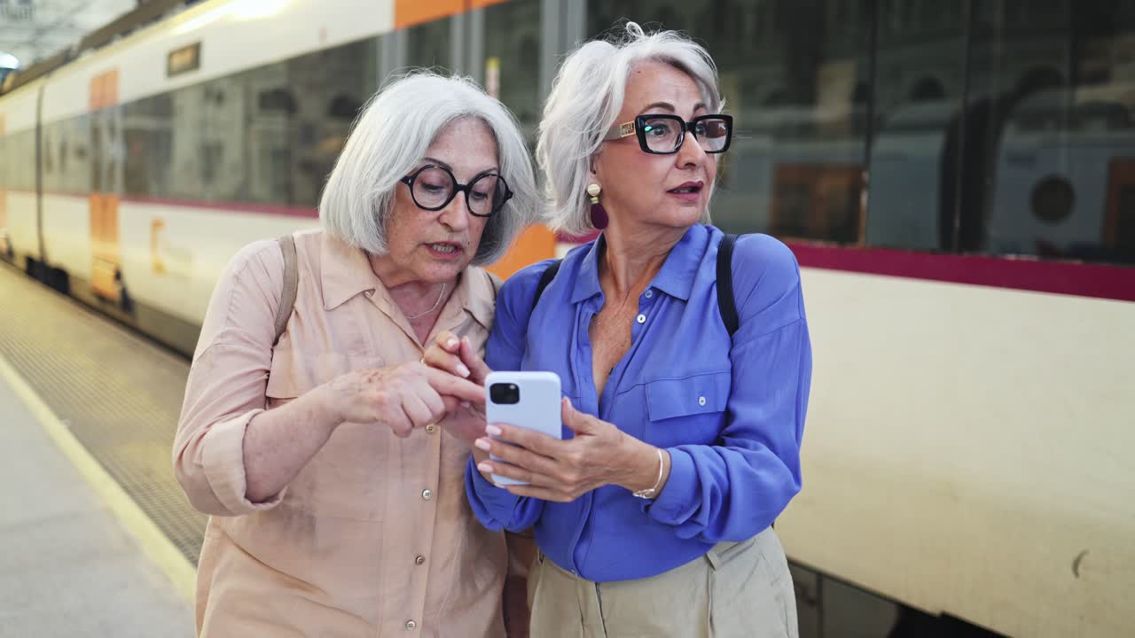 Due donne anziane che discutono di qualcosa su uno smartphone in una stazione ferroviaria