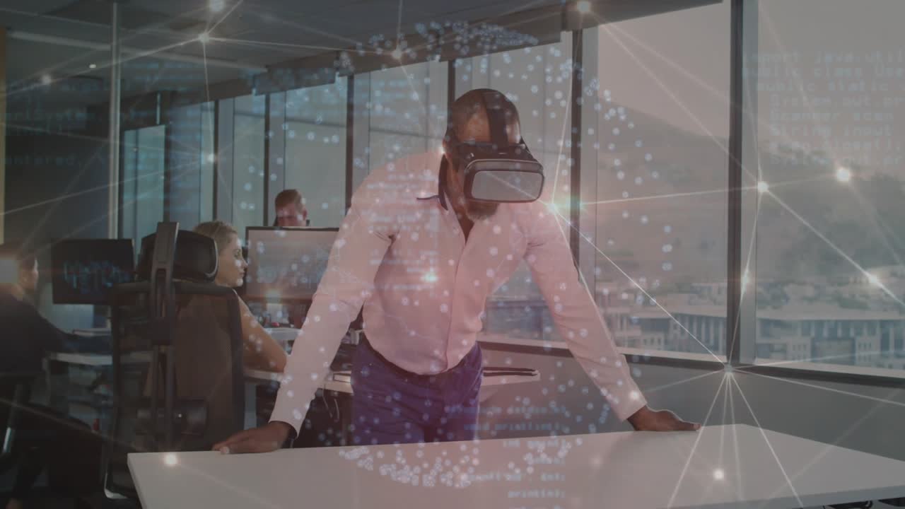Mand med VR-headset ved skrivebord med kolleger, der skriver blandt flydende kodeoverlejringer på et teknisk kontor