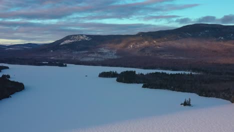 aerial slide over a frozen lake with islands, a large mountain, and pink clouds