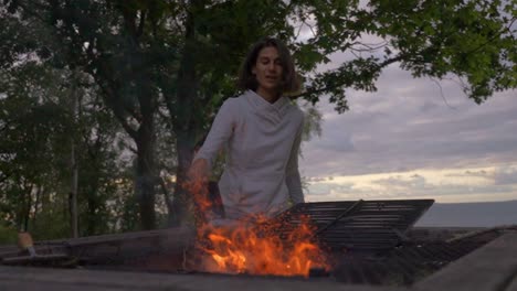 a person throwing coal into a fire with flames rising, in a serene outdoor setting