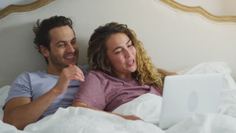 una pareja enamorada con pijama acostada en la cama en casa haciendo una llamada de video en la computadora portátil
