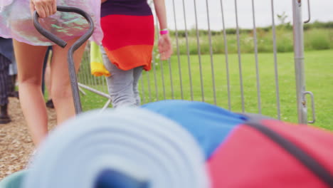 group of excited young friends at music festival carrying camping equipment onto site