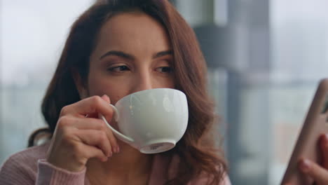 mujer de la mañana leyendo sms de teléfono móvil en la cocina de primer plano. dama bebiendo café