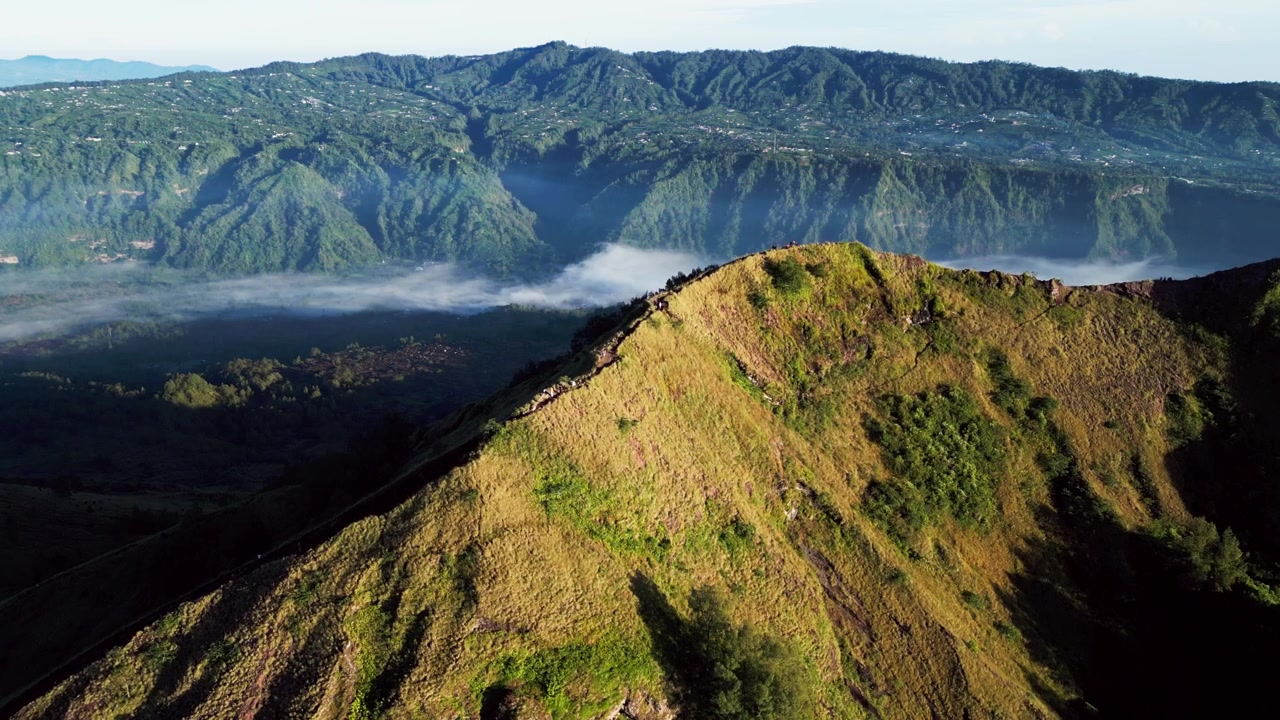 Escursionisti in piedi sopra un'ampia conca calderica e aspre creste montuose durante la luce dorata del mattino presso un panoramico punto di osservazione del cratere vulcanico, filmato aereo con drone con movimento in avanti