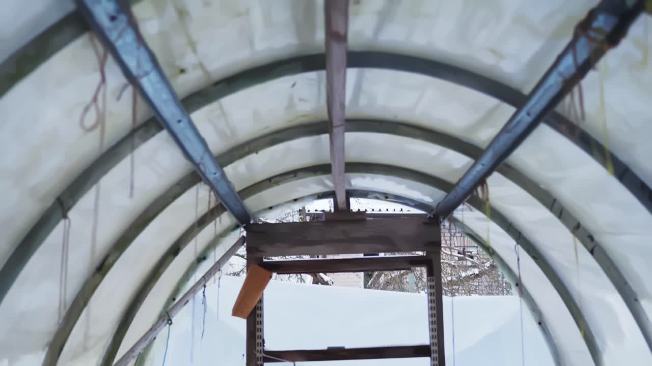Wnętrze zimowego tunelu foliowego z grządkami pokrytymi liśćmi, wiadrem i pustymi doniczkami, ukazujące przygotowania do sezonu poza sezonem, dawny wiejski styl życia i porządki w ogrodzie