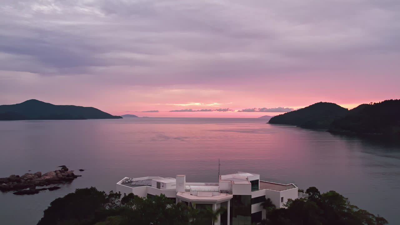 Dramatic sunset. Aerial flying backwards revealing mansion on the rocky coast island