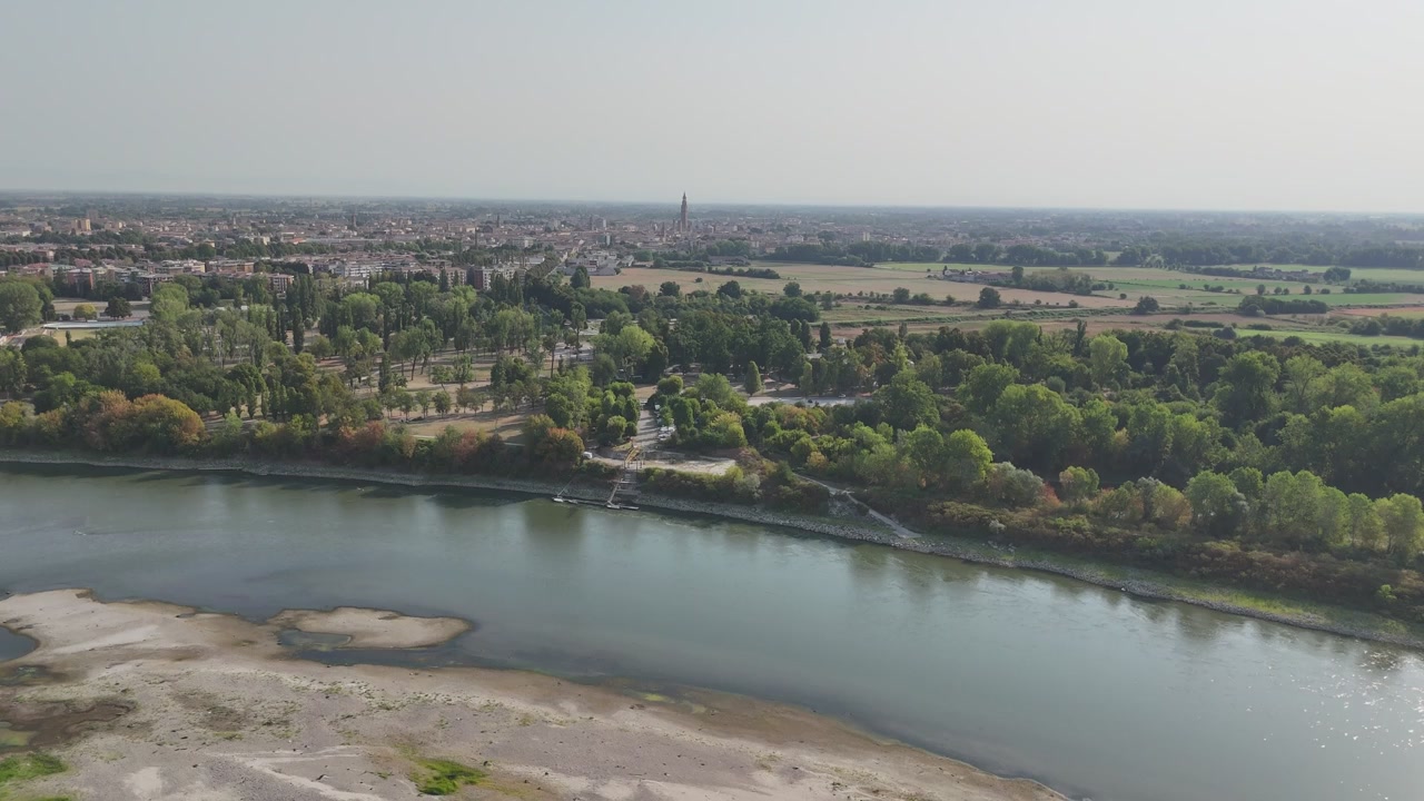 El río Po expone amplios bancos de arena a un nivel mínimo récord junto a Cremona, con el Torrazzo elevándose en el horizonte distante durante la ola de calor de 2026, toma de dron en retroceso.