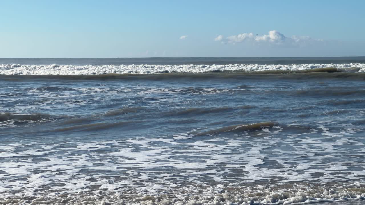 Inquadratura fissa di forti onde oceaniche che si infrangono sulla riva sotto un cielo azzurro limpido a Barbate, Spagna, paesaggio costiero naturale.