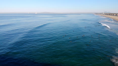 Breiter-4k-HD-Drohnenschub-Aus-Der-Luft,-Überführung-Vom-Huntington-Beach-Pier-Zu-Einer-Großen-Gruppe-Von-Surfern-Im-Sonnigen,-Blauen-Pazifischen-Ozean,-Südkalifornien-Am-Frühen-Morgen