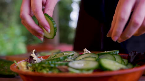 Picking-up-cucumber-slices-from-cutting-board-and-putting-on-salad-bowl