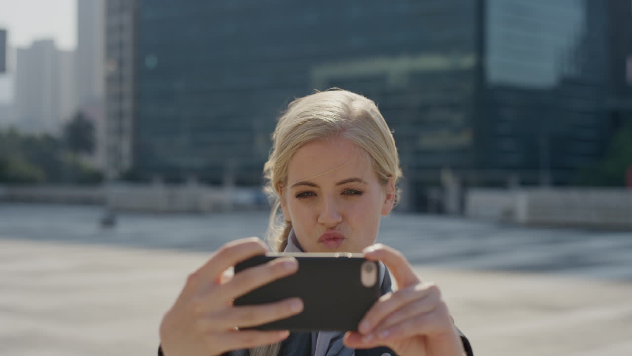 retrato de una joven rubia feliz que usa un teléfono inteligente tomando una foto selfie haciendo caras en la ciudad disfrutando de un estilo de vida urbano independiente