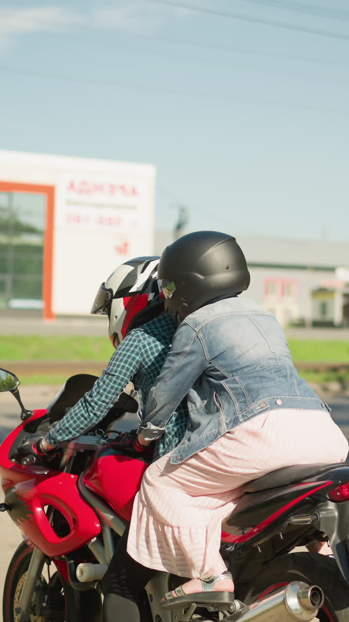 체크색 셔츠를 입은 여자가 은 자전거를 타고 그녀의 친구와 함께 뒤에서 그녀를 붙잡고, 둘 다 헬을 착용하고, 에 나무가 있고, 유리로 먼 건물을 타고 있습니다.