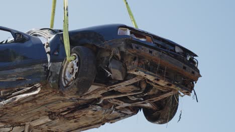 coche de accidente destrozado siendo levantado con cinturones en el depósito de chatarra