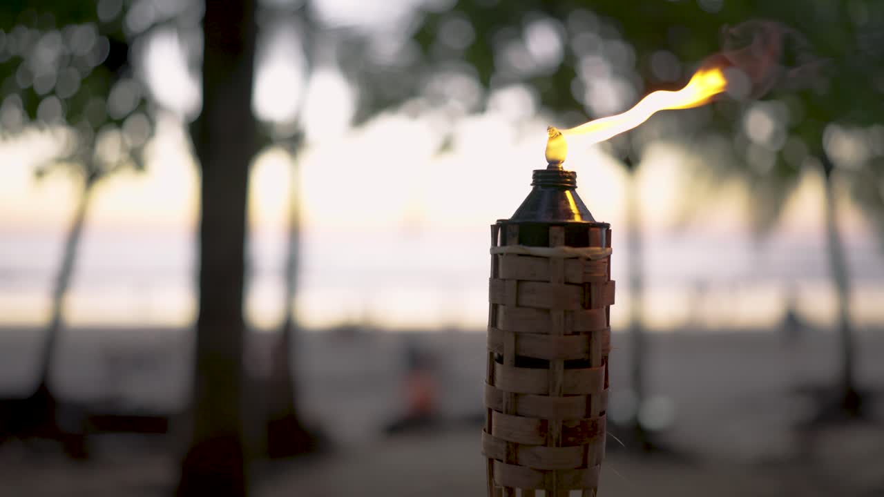 Torcia tiki con fiamma tremolante su una spiaggia tropicale al tramonto