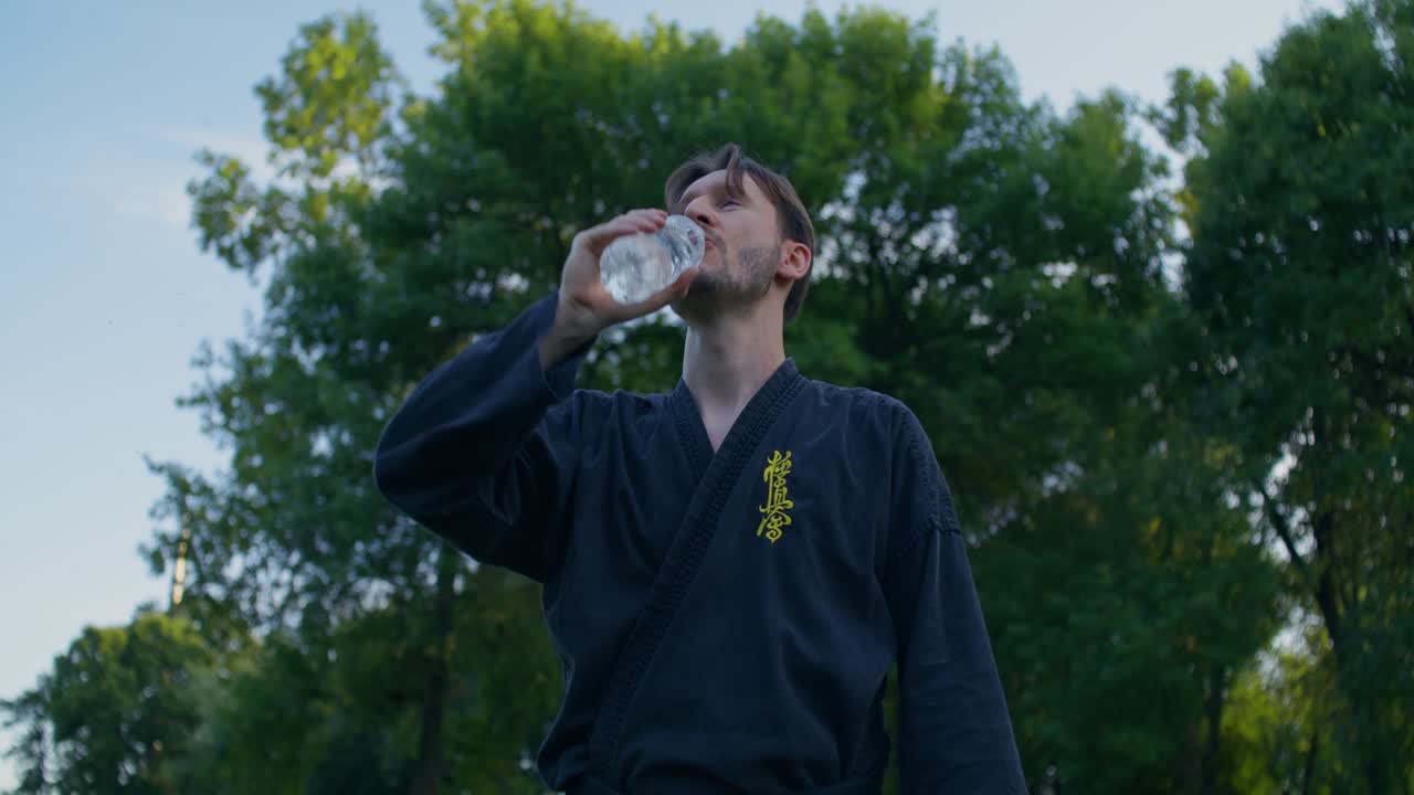 Uomo in tenuta da karate che beve acqua al parco