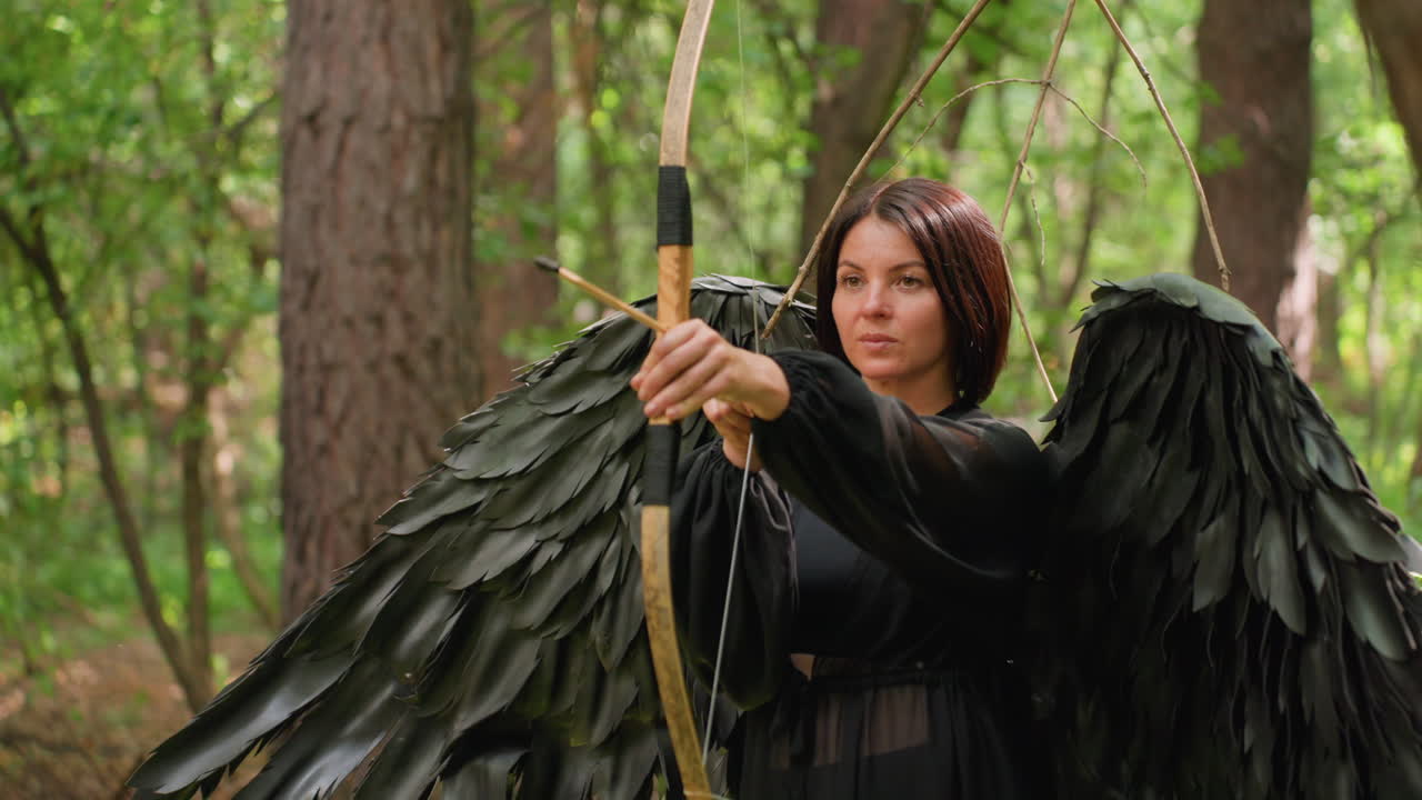 Forest guardian dressed in black with large dark wings stands among trees holding bow, looking serious and focused before shooting arrow, symbolizing strength and mystic nature spirit presence