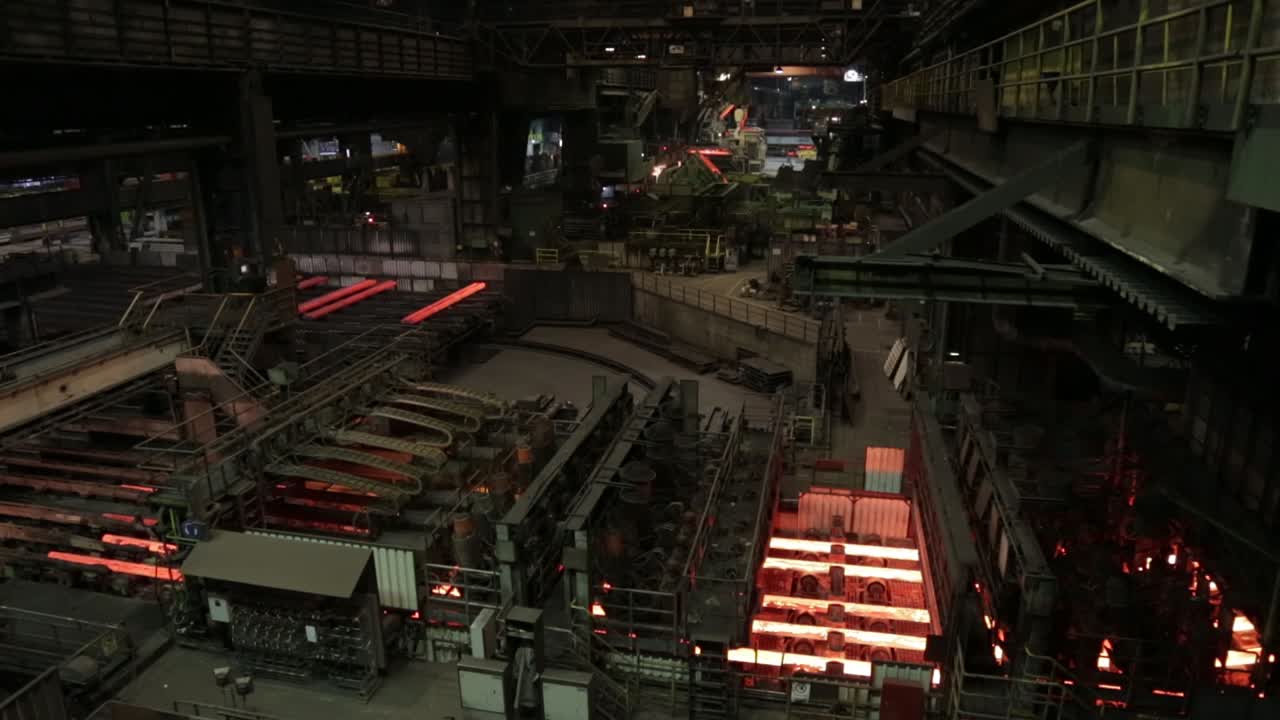 A steel mill with molten metal on conveyor belts in a dark, industrial setting