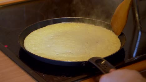 flipping a pancake with wooden spatula in a frying pan