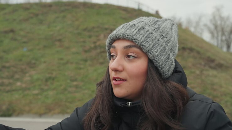 Prove di danza all'aperto con calzature testurizzate. Una donna con un cappello di lana ispeziona la suola dello stivale in un parco. Una ballerina che si prepara a passi giocosi mentre esamina il battistrada fangoso sulle sue scarpe da sentiero.