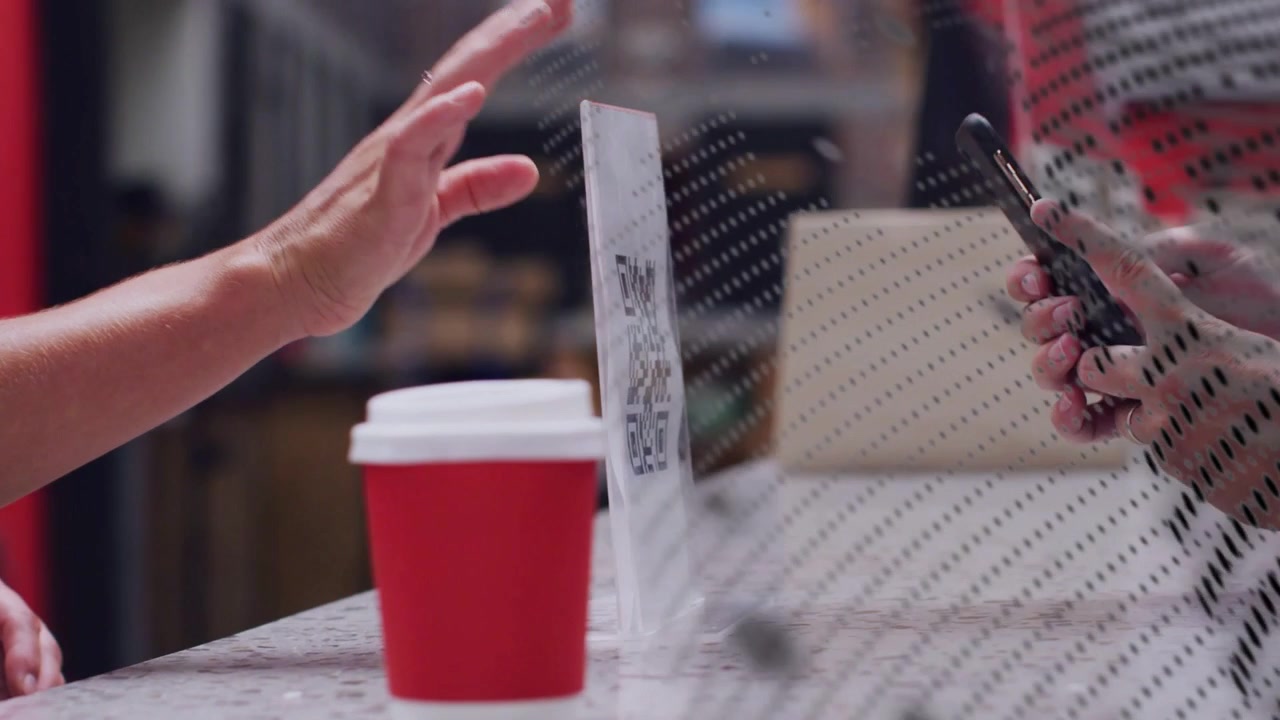 Mano che posiziona una tazza sul bancone, utente di telefono che scansiona un codice QR attraverso uno schermo puntinato per il pagamento