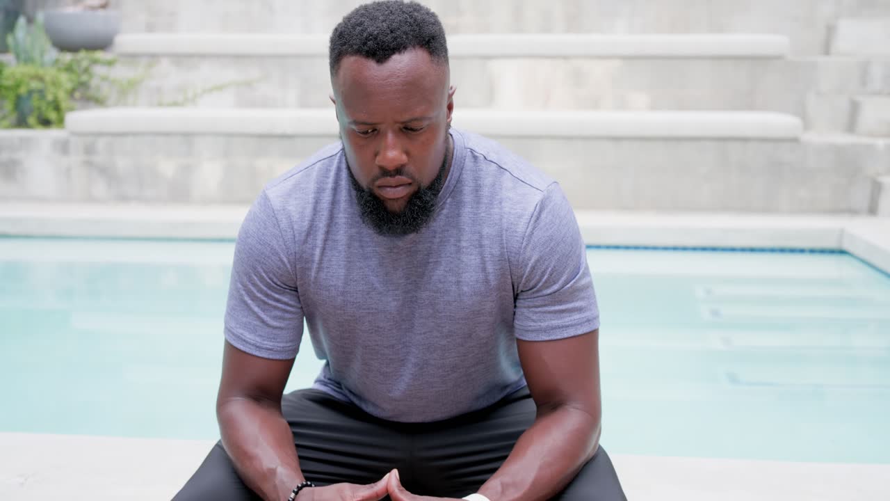 African man sitting on pool coping wearing smartwatch, camera zooming, lifting head meeting lens