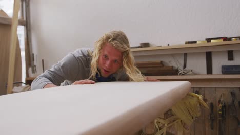 caucasian male surfboard maker making a surfboard and preparing to polishing