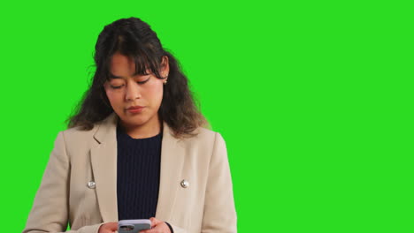 Close-Up-Studio-Shot-Of-Businesswoman-Using-Mobile-Phone-To-Message-Or-Browse-Online-Standing-Against-Green-Screen