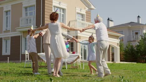 family dancing and applauding for grandmother on birthday party outdoors