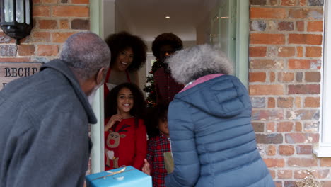 grandparents being greeted by family as they arrive for visit on christmas day with gifts