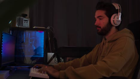 Male-using-PC-gaming-and-concentrating-while-wearing-white-headphones-in-a-darkened-room